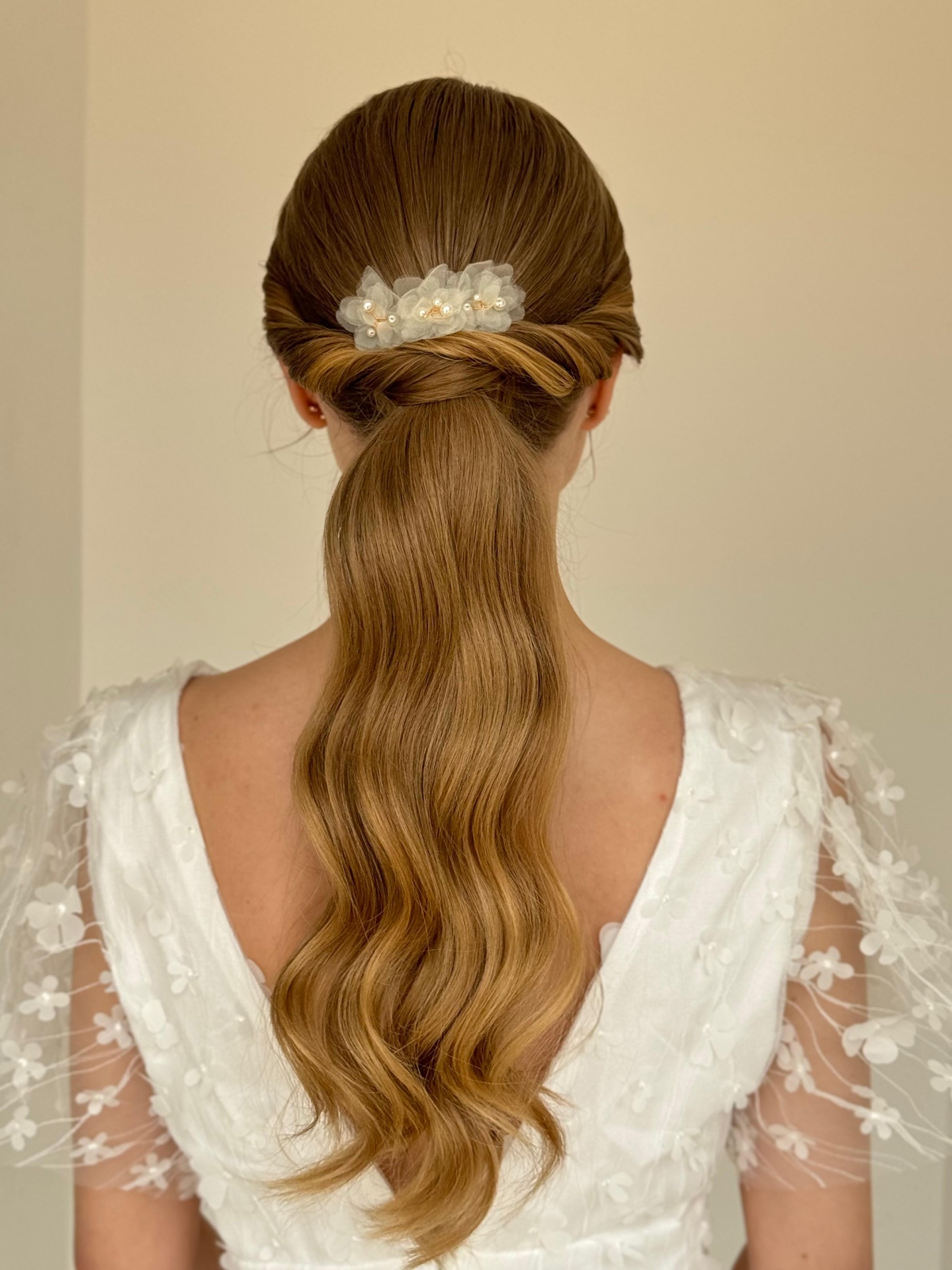 Penteado de noiva com rabo de cavalo ondulado e acessório floral