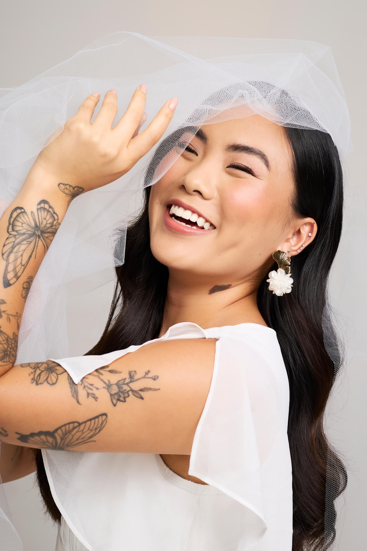 Noiva sorrindo com véu, tatuagens delicadas e brincos dourados